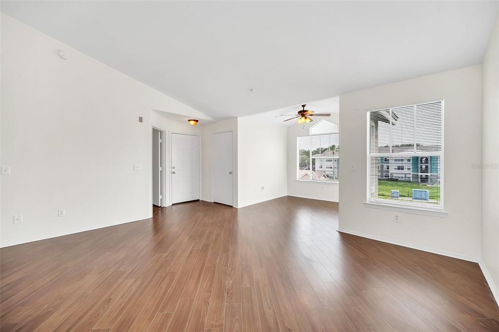 An empty living room features wood-look flooring, white walls, and a large window — 2210 GRAND CAYMAN COURT UNIT 1735, KISSIMMEE, FL