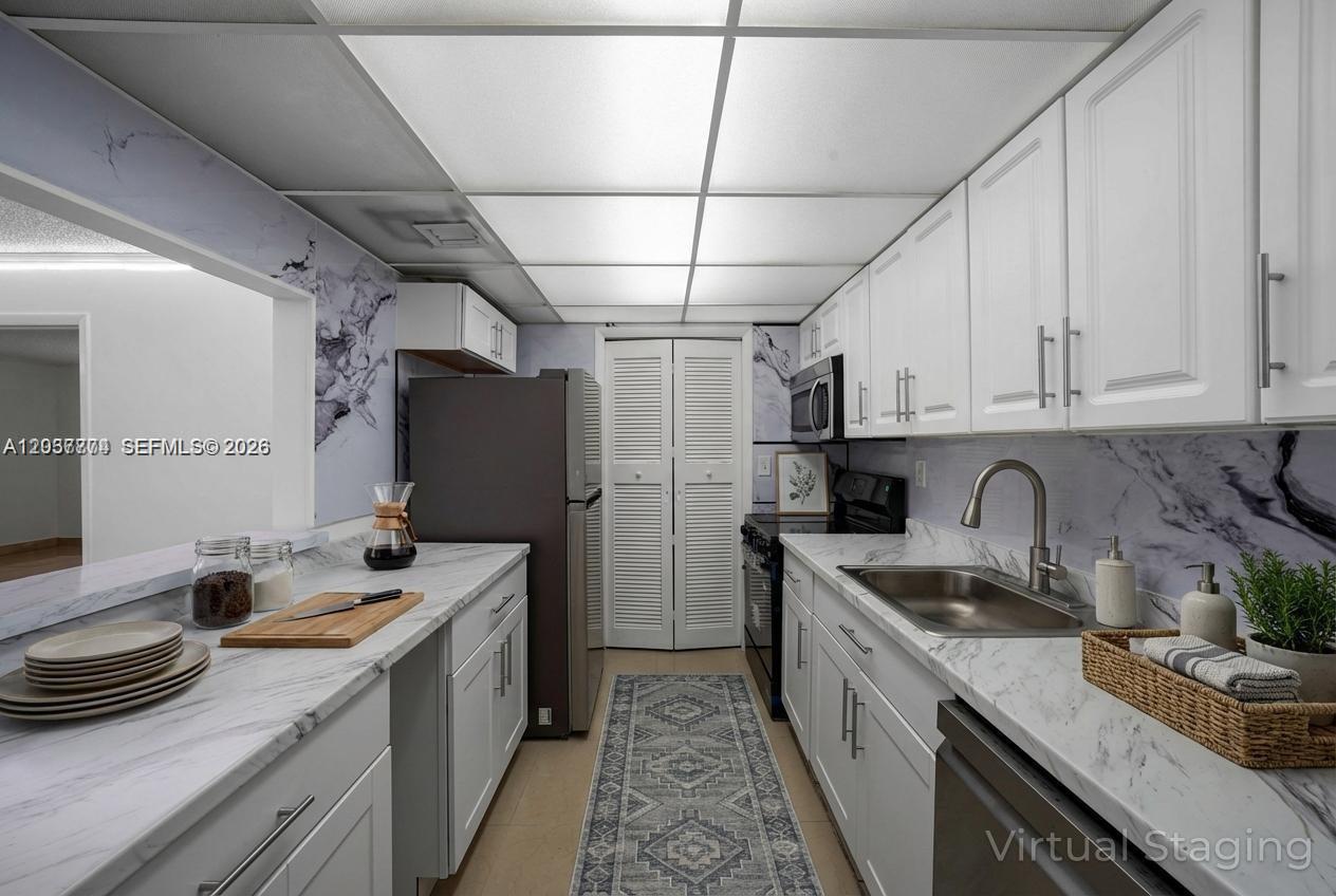 This galley kitchen features white cabinets, marble-patterned countertops, a stainless steel sink, and recessed lighting — 200 Lakeview Dr # 101, Weston FL 33326, WESTON, FL