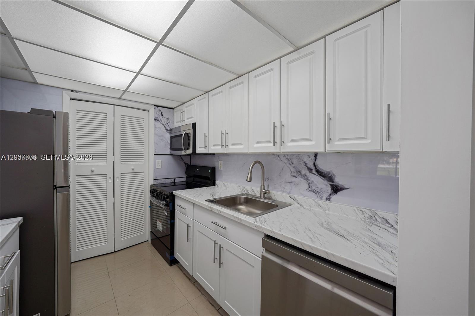 A kitchen features white cabinets, marble-patterned countertops, a stainless steel sink, and black appliances — 200 Lakeview Dr # 101, Weston FL 33326, WESTON, FL