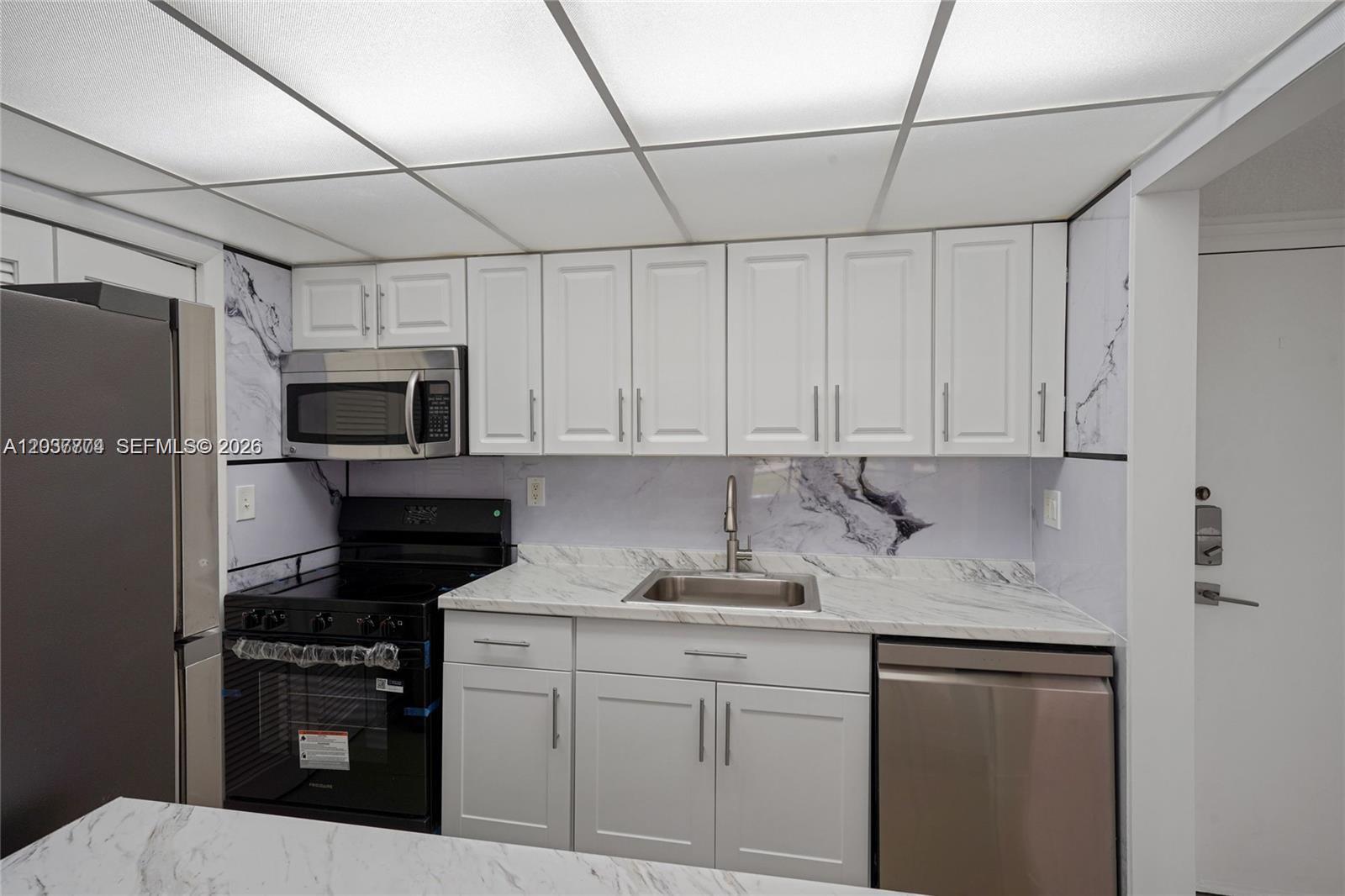 A kitchen features white cabinets, marble-patterned countertops, stainless steel appliances, and a drop ceiling — 200 Lakeview Dr # 101, Weston FL 33326, WESTON, FL