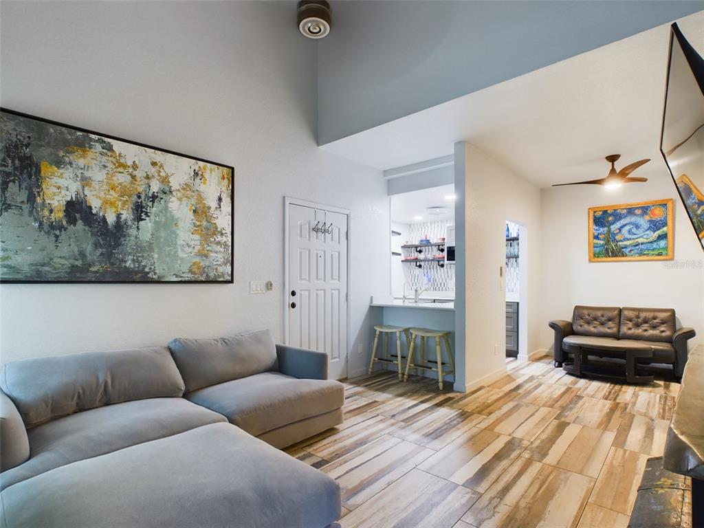 A living room with a gray sectional, wood-look tile floors, and a kitchen breakfast bar — 2049 SAN MARCOS DRIVE SE UNIT 127, WINTER HAVEN, FL