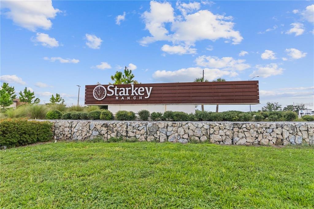 A large brown Starkey Ranch sign sits above a stone retaining wall in a grassy area — 11903 RANCHERS GAP DRIVE, ODESSA, FL