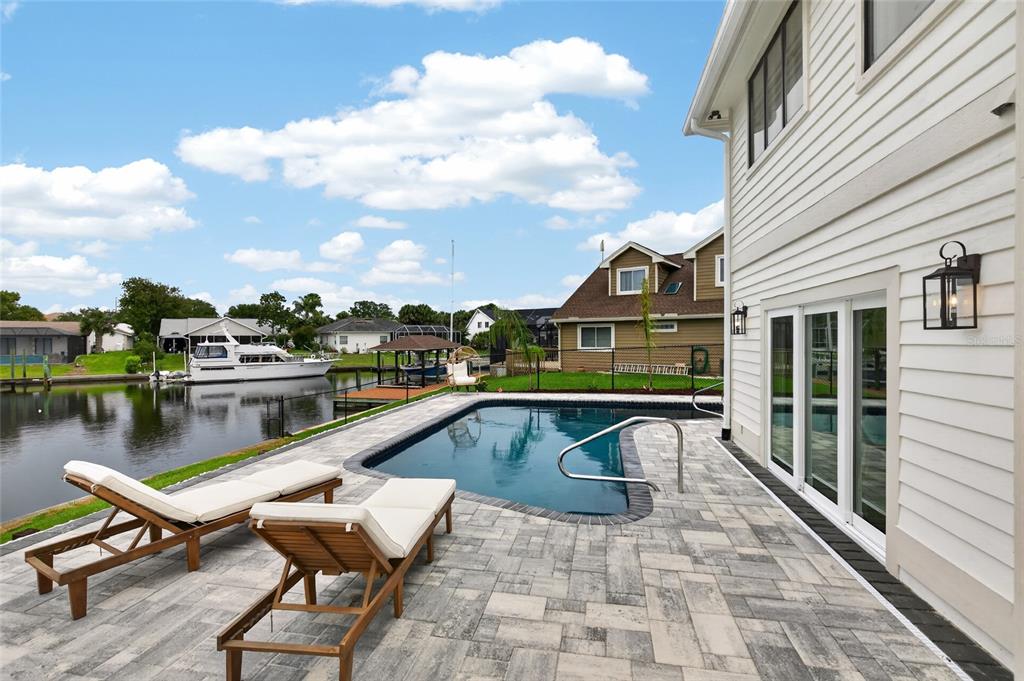 A backyard patio features a swimming pool, lounge chairs, and a view of a canal — 7 CHINOOK COURT, PALM COAST, FL