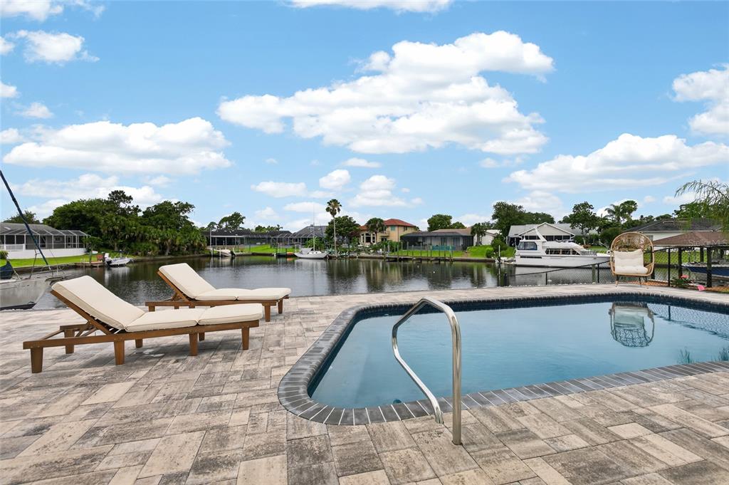 A swimming pool with lounge chairs overlooks a canal with docked boats under a blue sky — 7 CHINOOK COURT, PALM COAST, FL
