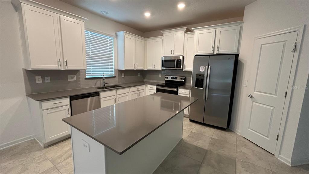 A modern kitchen features white cabinets, stainless steel appliances, and a large gray island countertop — 913 LAUREL VIEW WAY, GROVELAND, FL