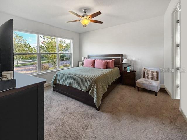 A bedroom features a bed with a green quilt, a ceiling fan, and large windows — 1305 LOMBARDI COURT, KISSIMMEE, FL