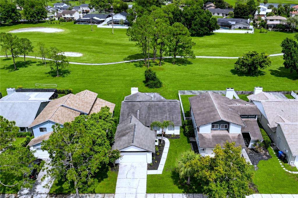 An aerial view shows three suburban houses with gray roofs bordering a large green golf course — 16131 GARDENDALE DRIVE, TAMPA, FL