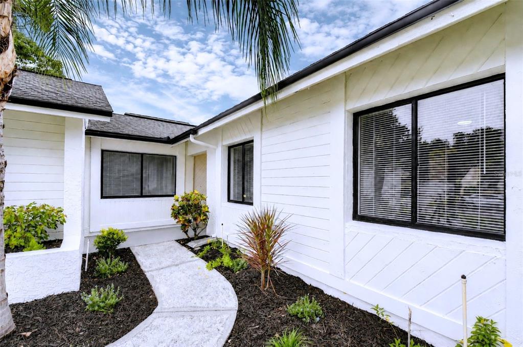 A white house exterior features a concrete walkway leading to the front entrance with landscaping — 16131 GARDENDALE DRIVE, TAMPA, FL