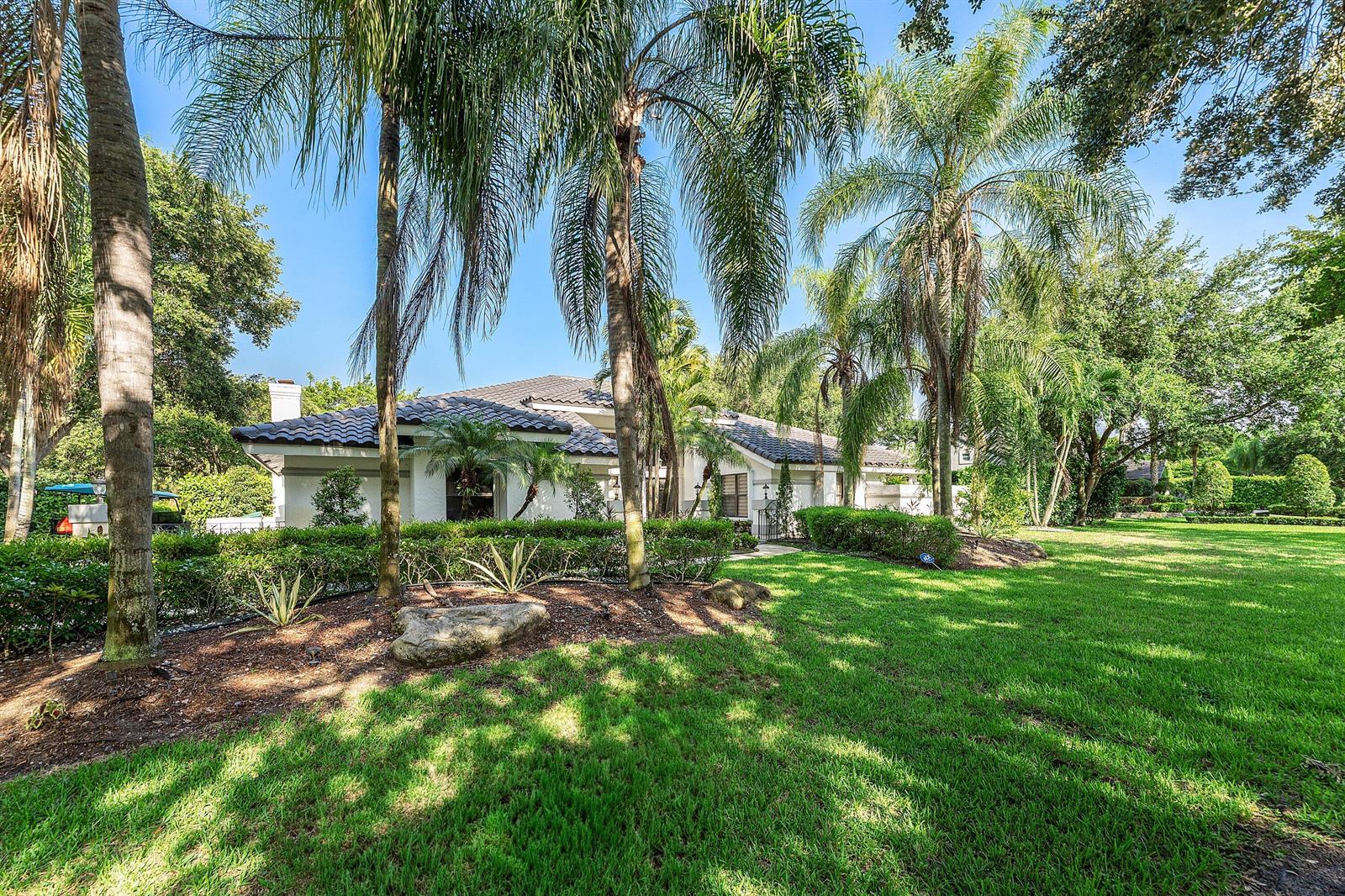 A white house with a tile roof sits behind a large lawn and palm trees — 7210 W Cypresshead Drive, Parkland FL 33067, PARKLAND, FL