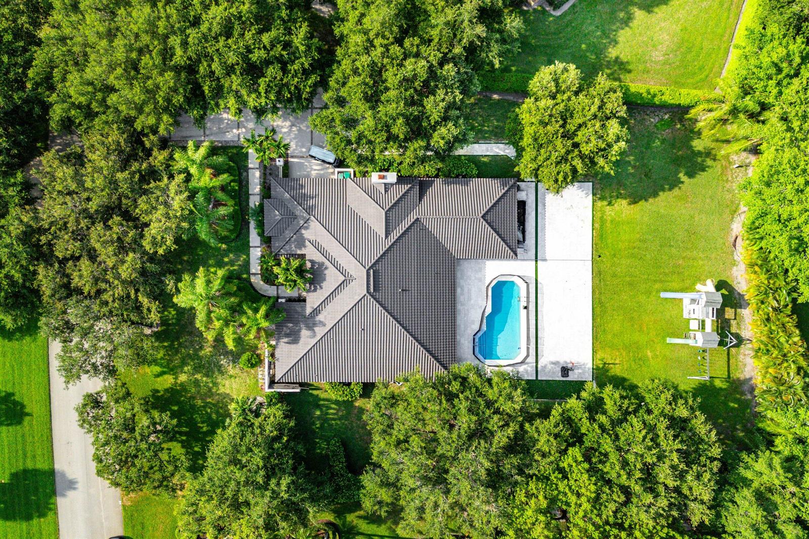 An aerial view shows a house with a dark tiled roof, pool, and backyard playground — 7210 W Cypresshead Drive, Parkland FL 33067, PARKLAND, FL