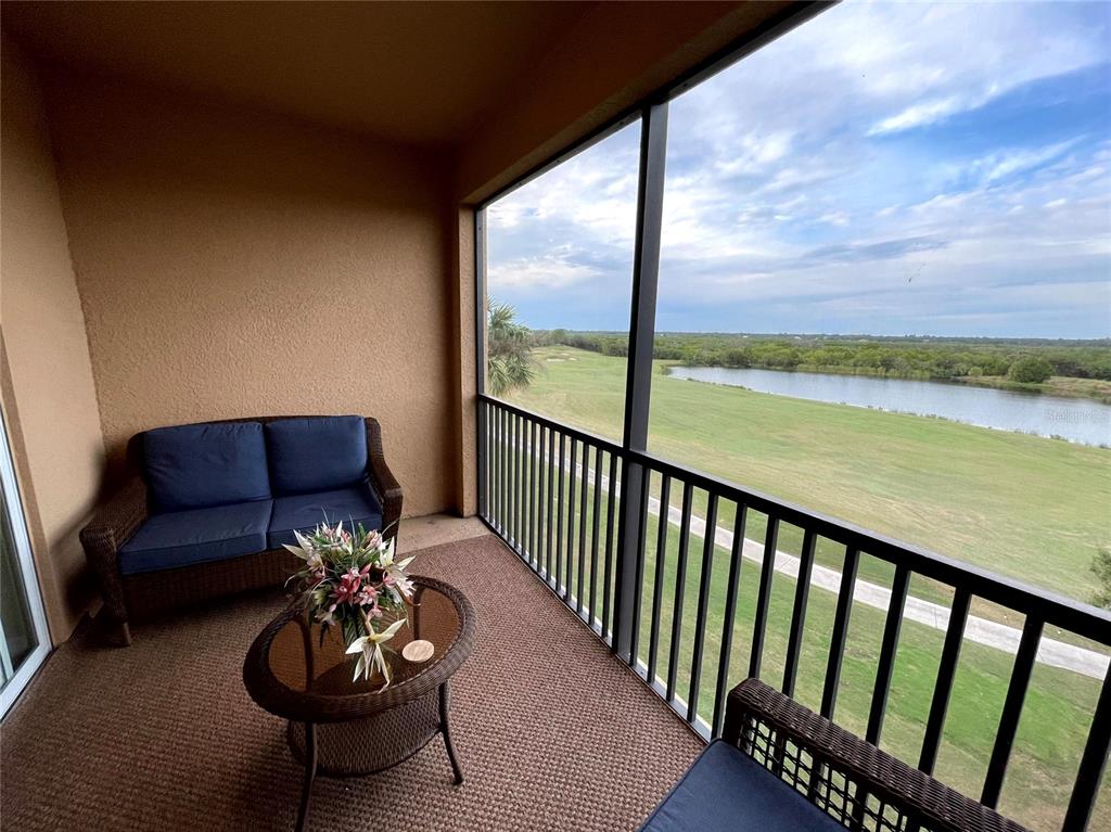 A screened-in balcony features wicker furniture overlooking a golf course and a pond — 8205 GRAND ESTUARY TRAIL UNIT 404, BRADENTON, FL