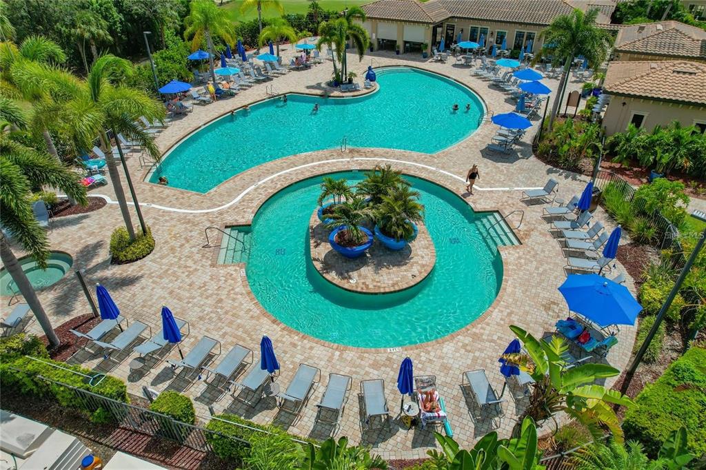 An aerial view of a resort-style swimming pool with lounge chairs and blue umbrellas — 8205 GRAND ESTUARY TRAIL UNIT 404, BRADENTON, FL