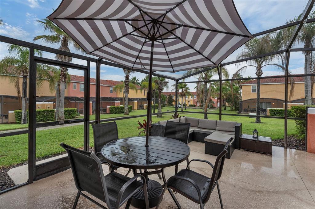A screened-in patio features a dining set, an umbrella, and outdoor sectional seating — 3023 RED GINGER ROAD, KISSIMMEE, FL