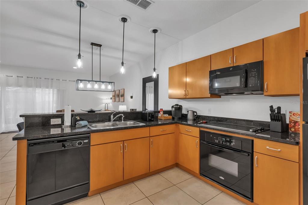 A kitchen features light wood cabinets, black appliances, and dark granite countertops — 3023 RED GINGER ROAD, KISSIMMEE, FL