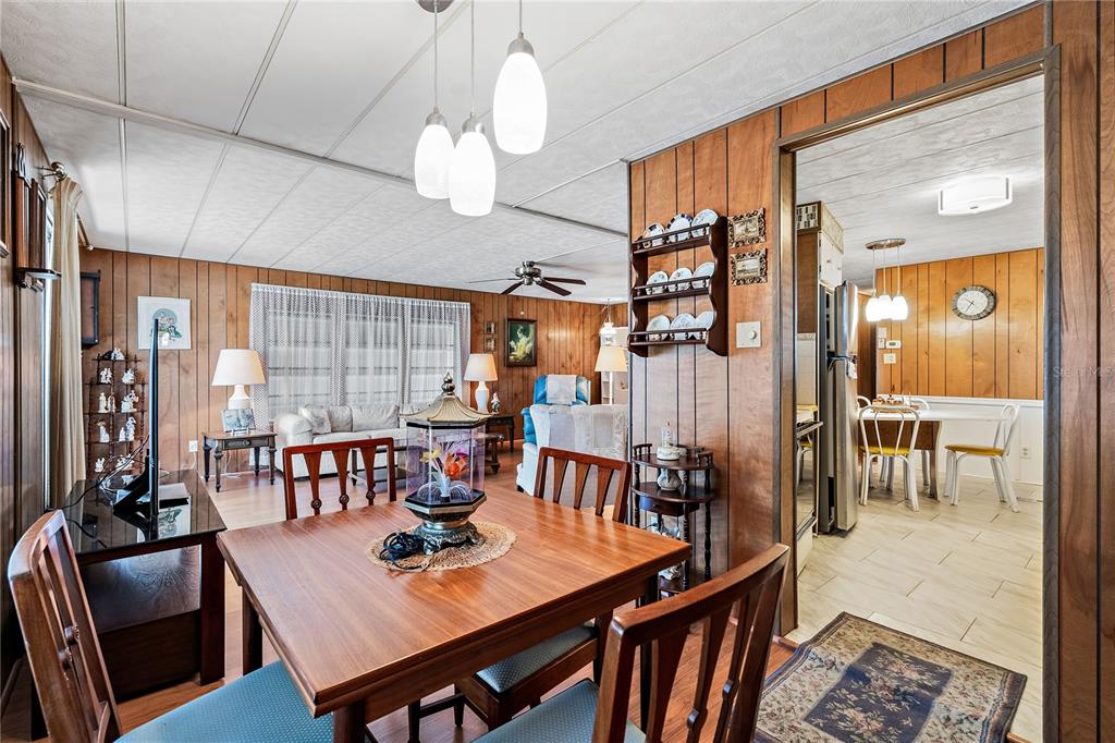 A dining area with wood paneling leads into a living room and a kitchen beyond — 3410 SPANISH OAK TERRACE, SARASOTA, FL