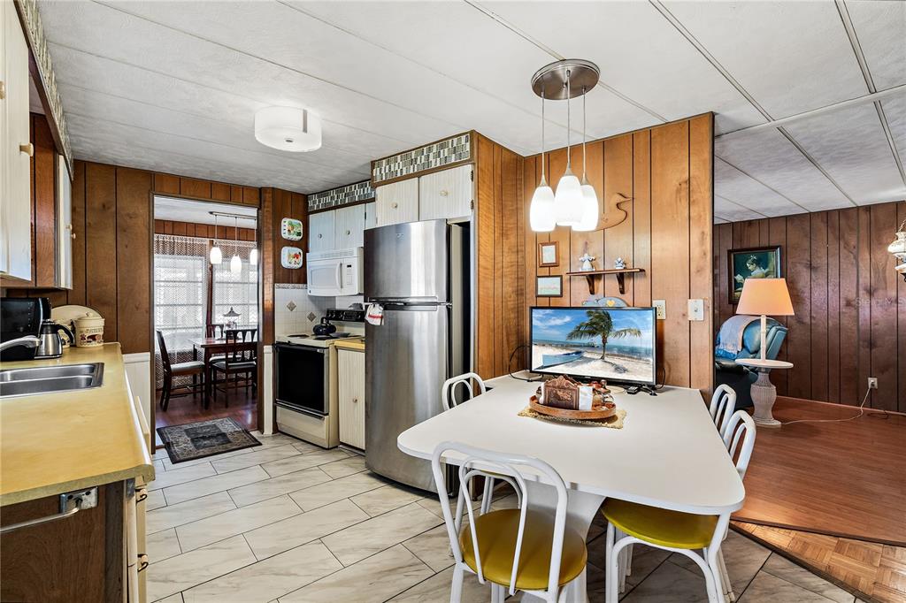 A kitchen with wood-paneled walls, stainless steel appliances, and a dining table with yellow chairs — 3410 SPANISH OAK TERRACE, SARASOTA, FL