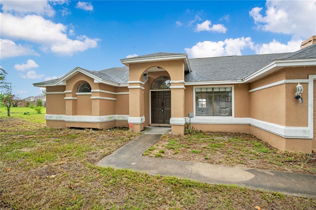 A tan, single-story stucco house features a covered entryway and a concrete walkway — 3210 PELL MELL DRIVE, ORLANDO, FL