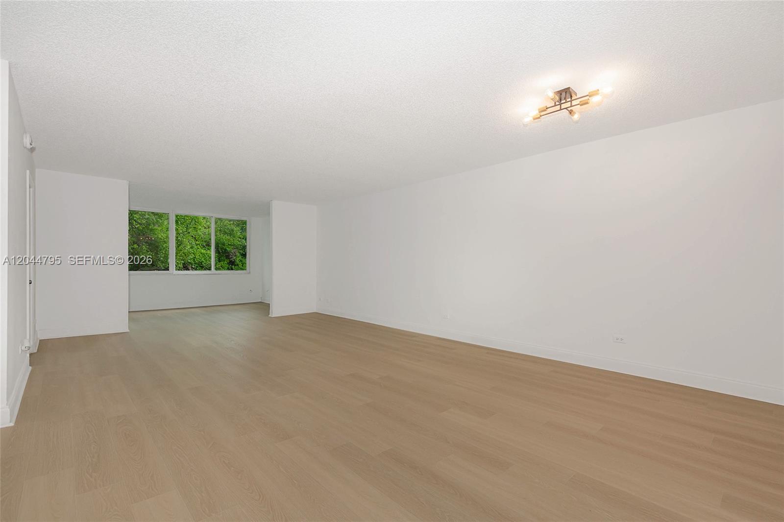 An empty room features light wood-look flooring, white walls, and a modern ceiling light fixture — 445 NE 195th St # 326, Miami FL 33179, MIAMI, FL