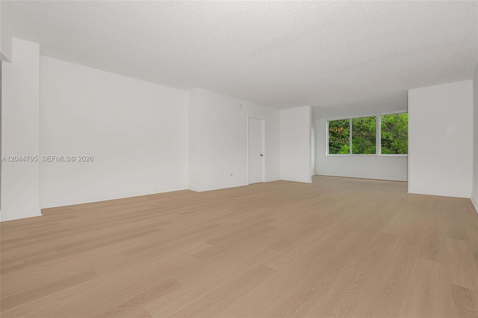 An empty room features light wood-look flooring, white walls, and a large window — 445 NE 195th St # 326, Miami FL 33179, MIAMI, FL