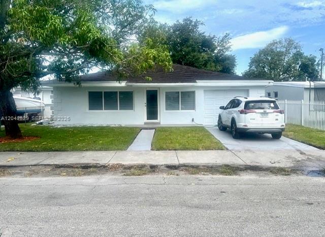 A white single-story house with a driveway and a parked SUV sits behind a lawn — 2390 Service Rd, Opa-Locka FL 33054, OPA-LOCKA, FL