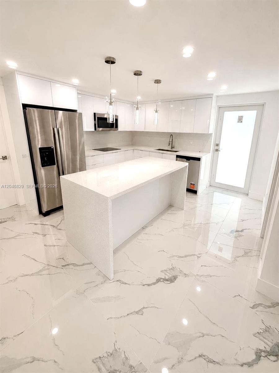A modern kitchen features white cabinetry, a quartz island, and marble-patterned tile flooring — 2390 Service Rd, Opa-Locka FL 33054, OPA-LOCKA, FL