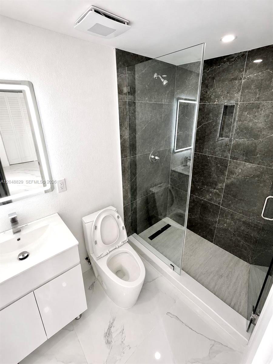 A modern bathroom features a white vanity, a toilet, and a glass-enclosed walk-in shower — 2390 Service Rd, Opa-Locka FL 33054, OPA-LOCKA, FL