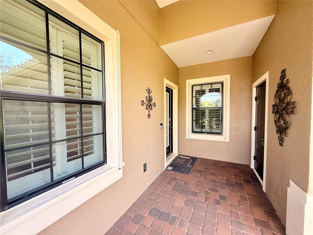 A covered entryway features a brick paver floor, two windows with shutters, and two doors — 10735 TROPHY DRIVE, ENGLEWOOD, FL