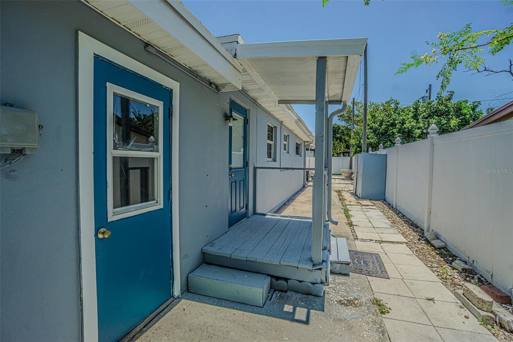 A side view of a house exterior featuring a blue door, wooden porch, and fence — 1627 28TH STREET N, ST PETERSBURG, FL