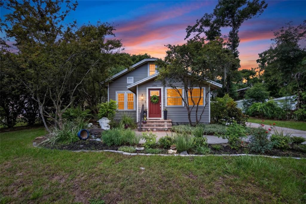A gray, single-story house with a red front door sits behind a landscaped front yard — 13941 13TH STREET, DADE CITY, FL