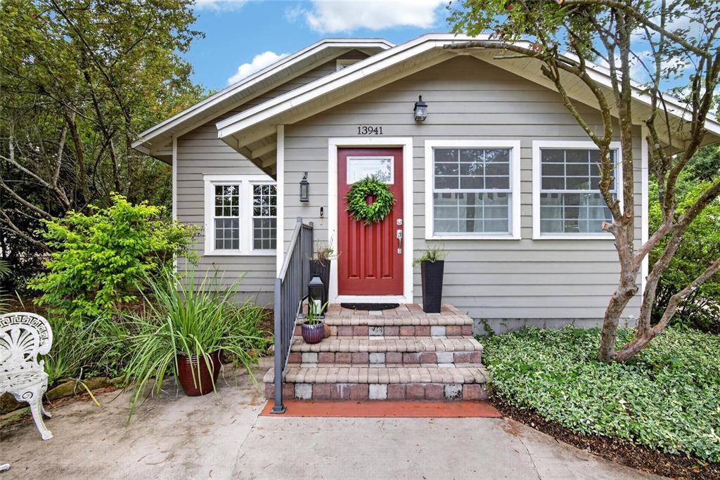 A gray house exterior features a red front door, brick steps, and a small porch — 13941 13TH STREET, DADE CITY, FL