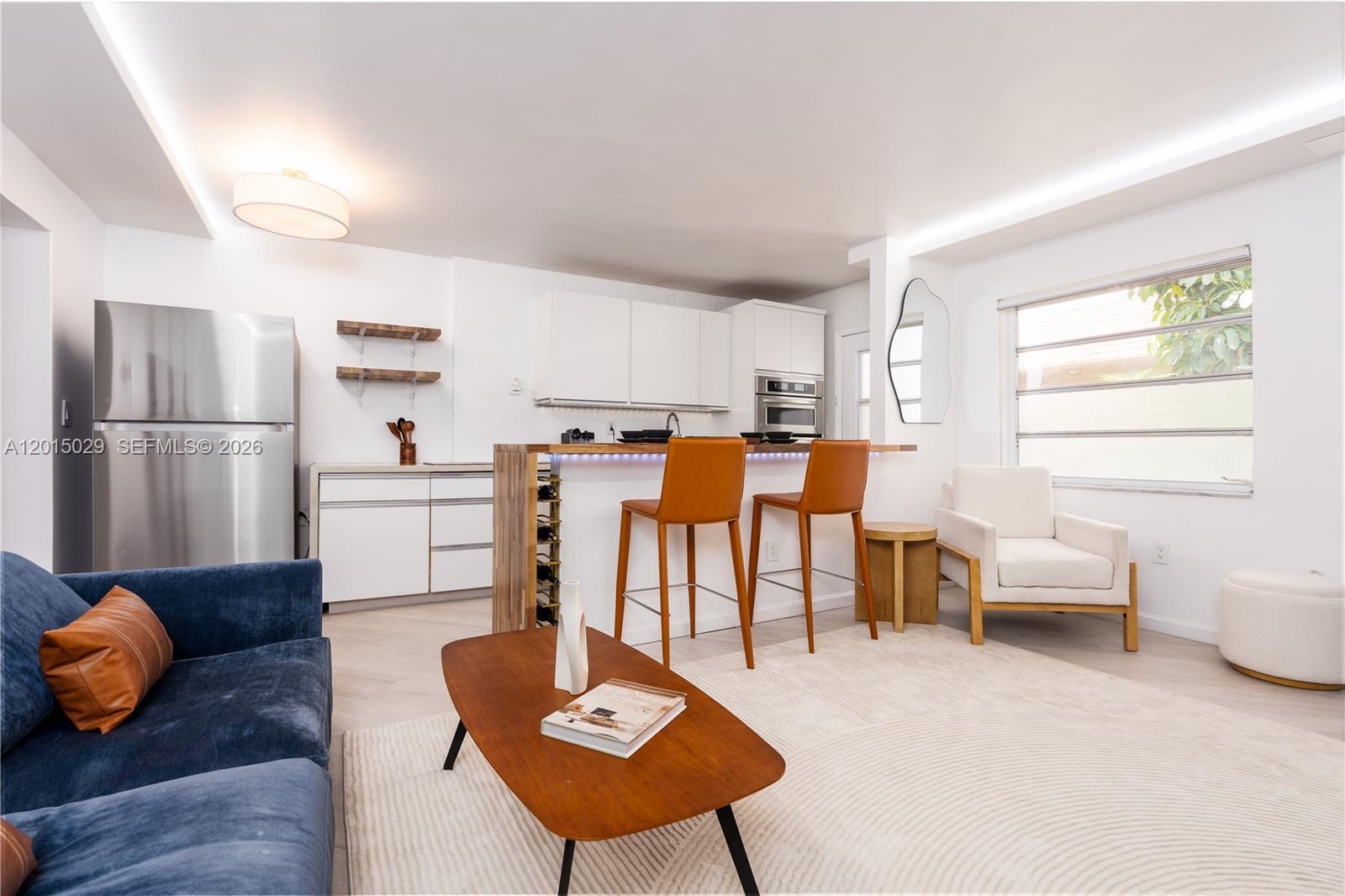 A modern open-concept kitchen and living area features white cabinetry, stainless appliances, and bar seating — 525 Meridian Ave # 203, Miami Beach FL 33139, MIAMI BEACH, FL