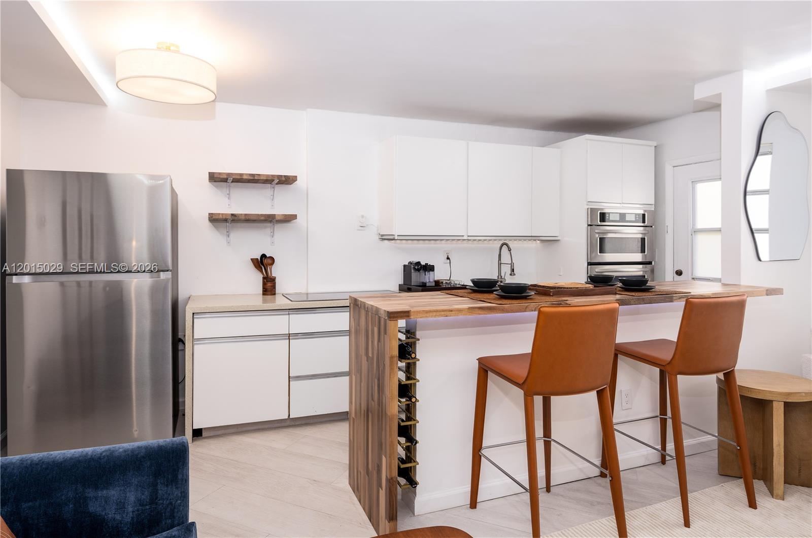 A modern kitchen features white cabinetry, stainless steel appliances, and a wooden breakfast bar — 525 Meridian Ave # 203, Miami Beach FL 33139, MIAMI BEACH, FL