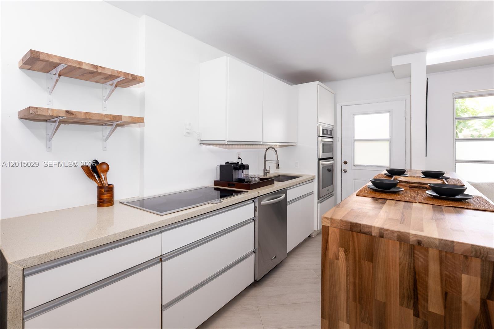 A modern kitchen features white cabinetry, a butcher block island, and floating wooden shelves — 525 Meridian Ave # 203, Miami Beach FL 33139, MIAMI BEACH, FL