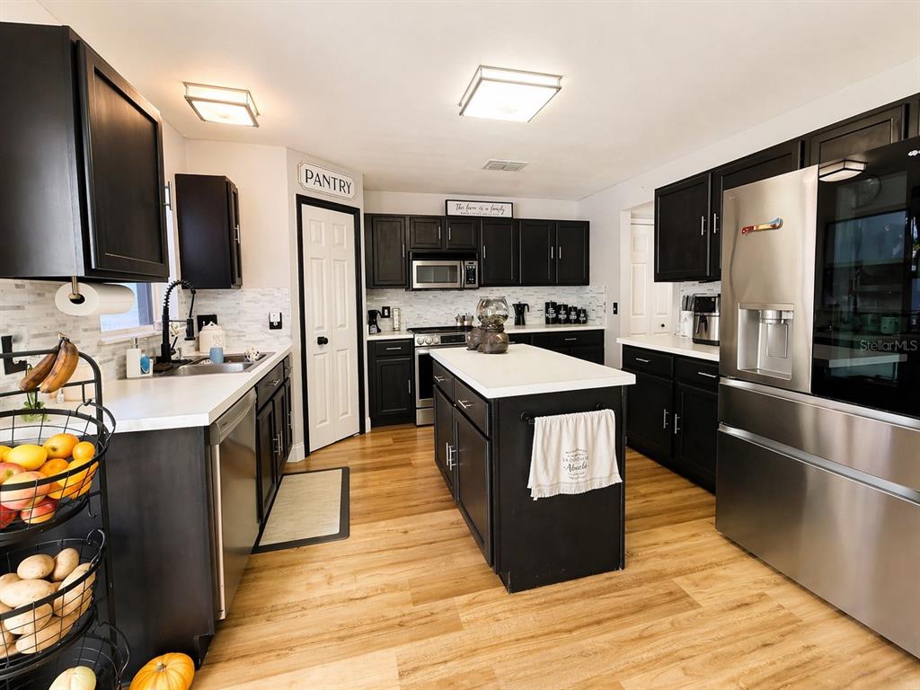 A kitchen features black cabinets, white countertops, stainless steel appliances, and light wood flooring — 3483 CHARMWOOD AVENUE, SPRING HILL, FL