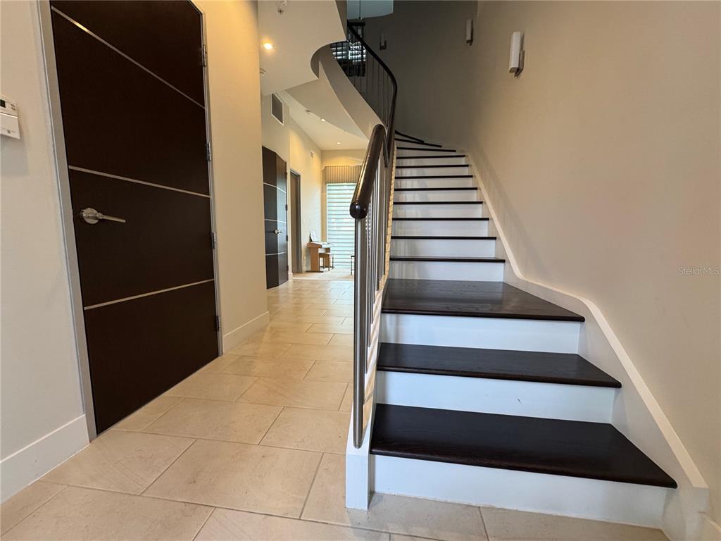 A staircase with dark wood treads and white risers leads to an upper floor — 239 COSMOPOLITAN COURT, SARASOTA, FL