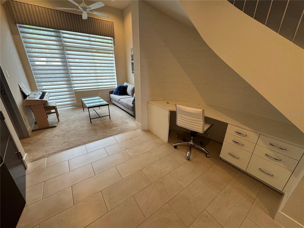 A room with tile flooring, a built-in desk under stairs, and an adjacent carpeted seating area — 239 COSMOPOLITAN COURT, SARASOTA, FL