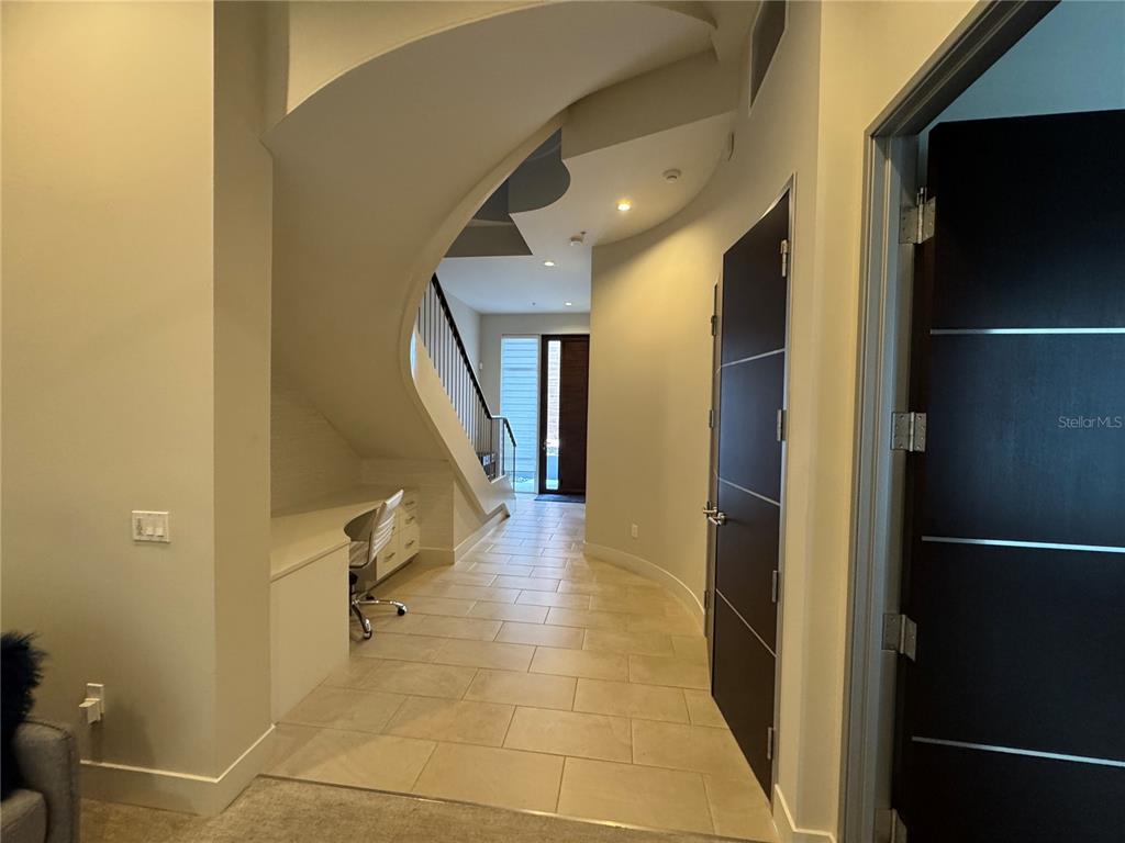 A hallway features a curved staircase, a built-in desk, tile flooring, and dark wood doors — 239 COSMOPOLITAN COURT, SARASOTA, FL