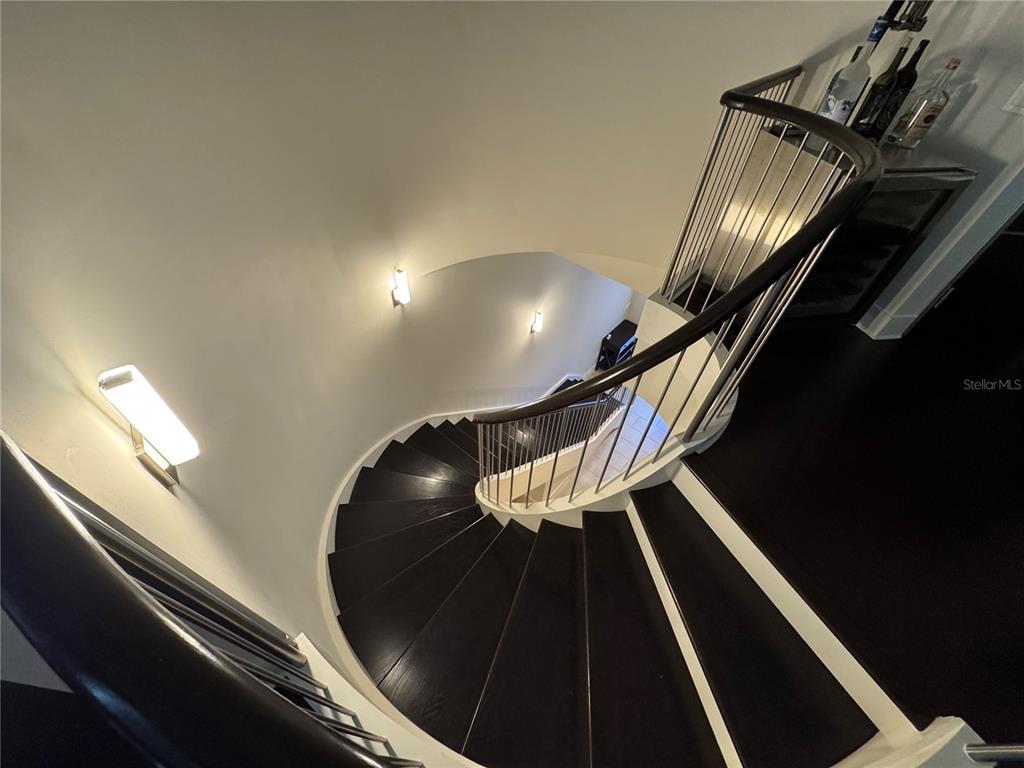 A curved wooden staircase with metal railings descends into a brightly lit interior space — 239 COSMOPOLITAN COURT, SARASOTA, FL