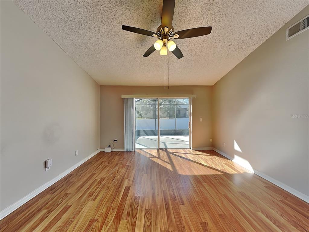 An empty living room features wood-look flooring, a ceiling fan, and sliding glass patio doors — 17128 WOODCREST WAY, CLERMONT, FL