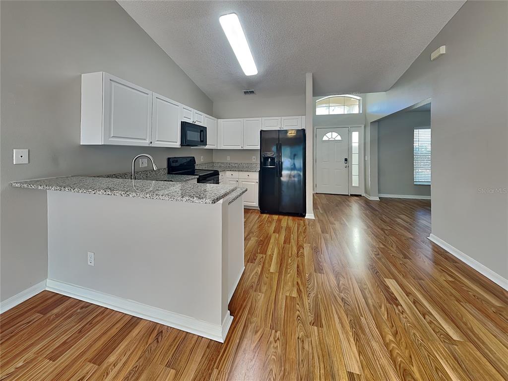 A kitchen with white cabinets, granite countertops, and black appliances overlooks a wood-floored living area — 17128 WOODCREST WAY, CLERMONT, FL
