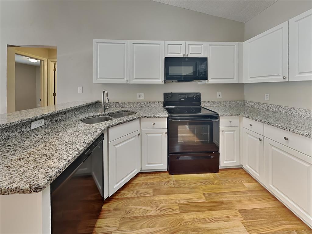 A kitchen features white cabinets, granite countertops, black appliances, and wood-look flooring — 17128 WOODCREST WAY, CLERMONT, FL
