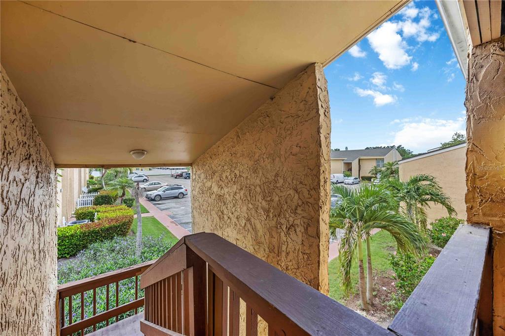 An outdoor staircase with a wooden railing overlooks a parking lot and palm trees — 3457 CLARK ROAD UNIT 255, SARASOTA, FL