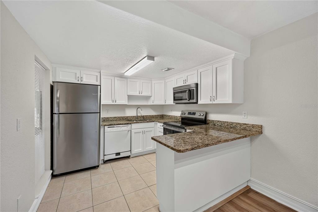 A kitchen with white cabinets, granite countertops, stainless steel appliances, and tile flooring — 3457 CLARK ROAD UNIT 255, SARASOTA, FL