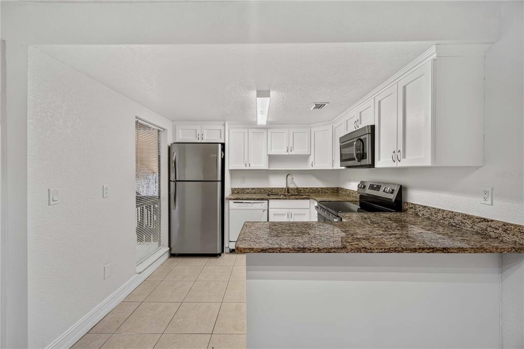 A kitchen features white cabinets, granite countertops, stainless steel appliances, and tile flooring — 3457 CLARK ROAD UNIT 255, SARASOTA, FL