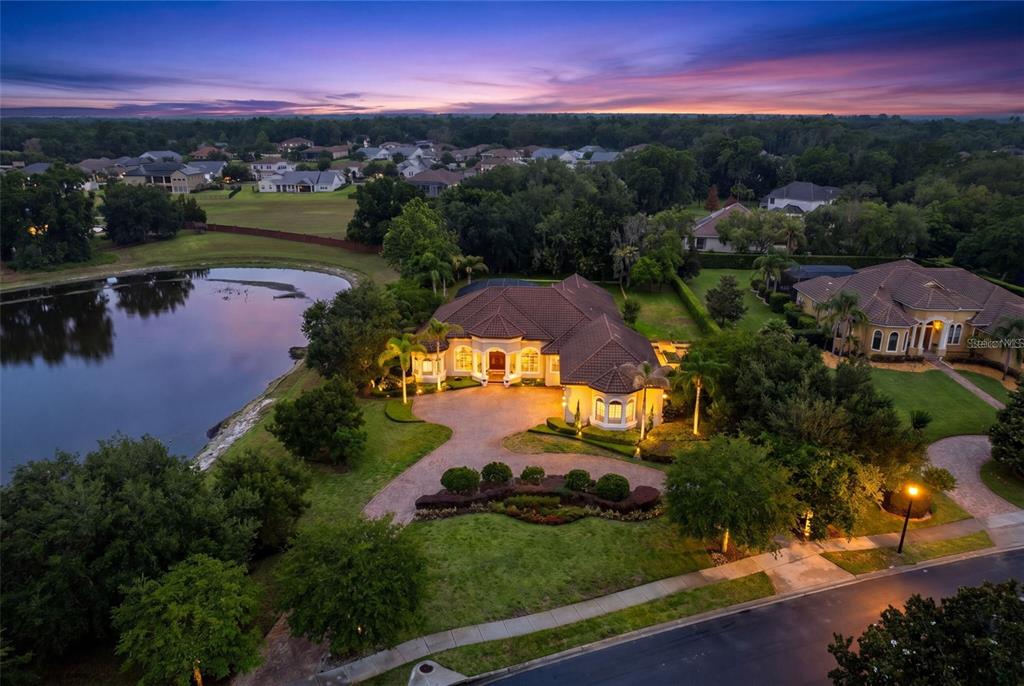An aerial view of a large house with a tile roof beside a lake at dusk — 1900 LAKE MARKHAM PRESERVE TRAIL, SANFORD, FL