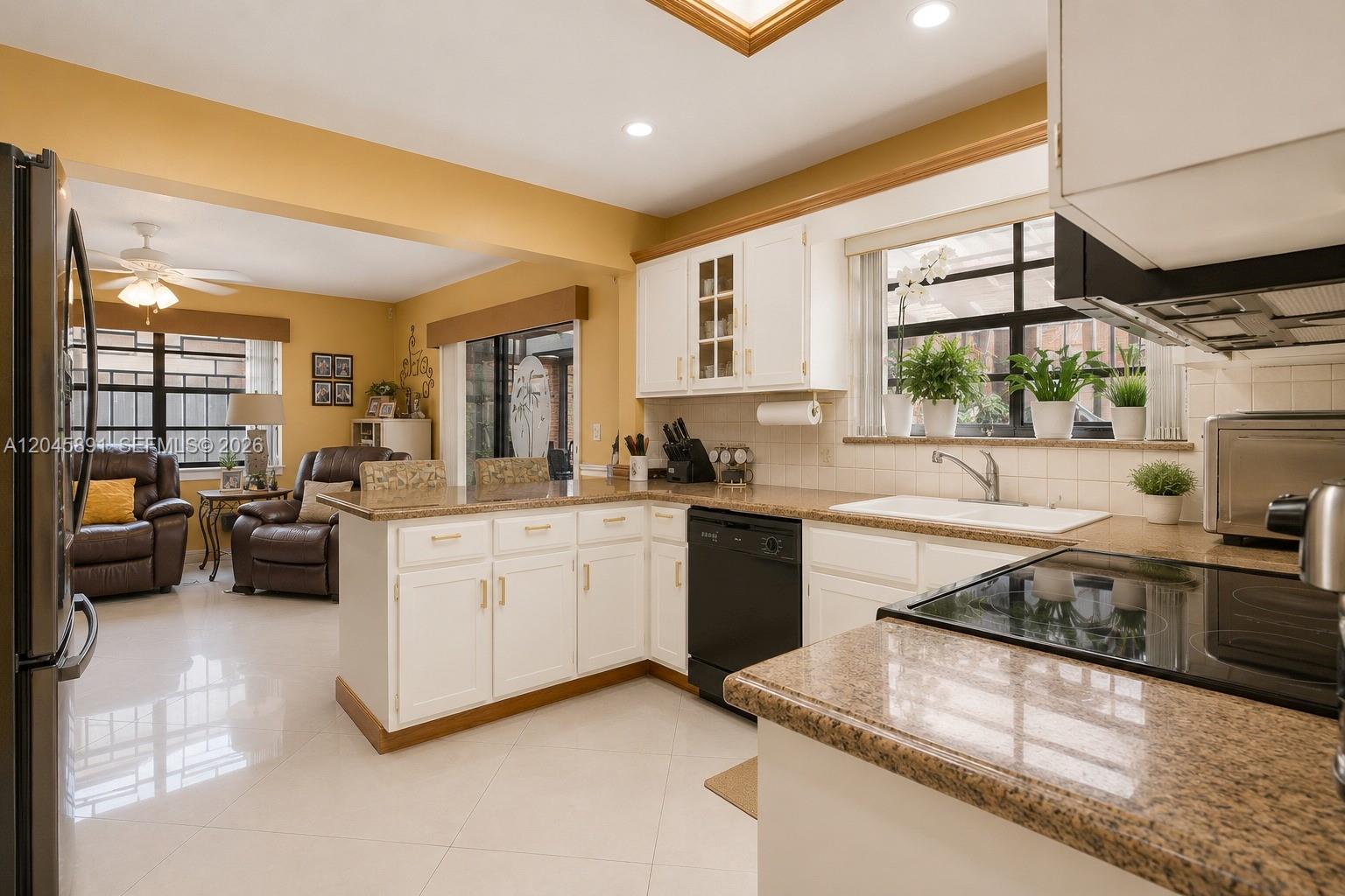A kitchen with white cabinets and granite countertops opens into a living area with tile floors — 520 NW 132nd Ct, Miami FL 33182, MIAMI, FL