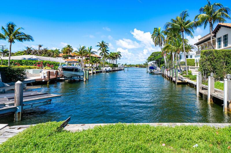 A canal view features boats docked at private piers lined with palm trees and houses — 102 Bonito Drive, Ocean Ridge FL 33435, OCEAN RIDGE, FL