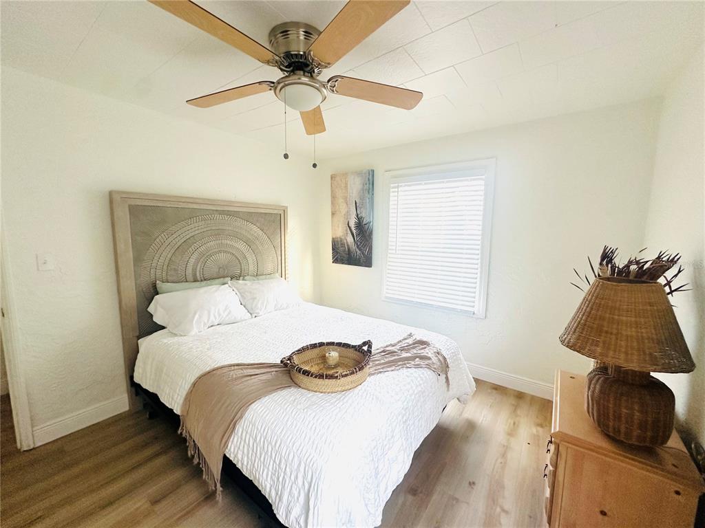 A bedroom features a bed with a textured headboard, a ceiling fan, and wood flooring — 4811 EMERSON AVENUE S, ST PETERSBURG, FL