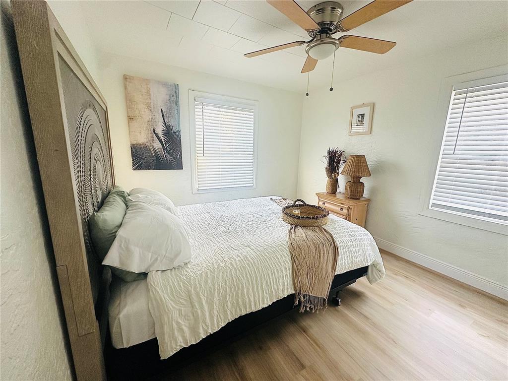A bedroom features a bed with a textured headboard, light wood flooring, and two windows — 4811 EMERSON AVENUE S, ST PETERSBURG, FL