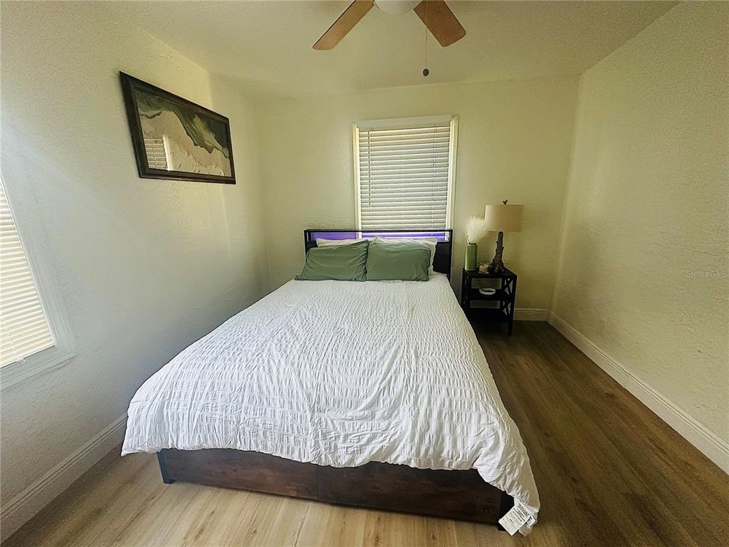 A bedroom features a bed with a white comforter, wood-look flooring, and a ceiling fan — 4811 EMERSON AVENUE S, ST PETERSBURG, FL